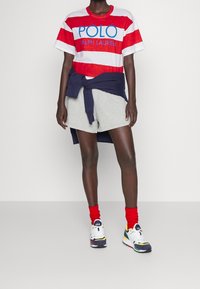 Röd och vit randig t-shirt med texten "POLO RALPH LAUREN", gråa shorts, blå tröja knuten runt midjan, röda strumpor, färgglada sneakers.