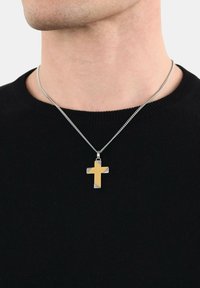 Collana in argento con pendente a croce in oro e argento, caratterizzata da un design elegante e una texture liscia, indossata sopra un maglione nero.