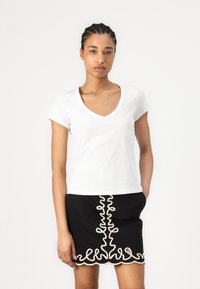 T-shirt blanc à manches courtes et décolleté en V associé à une jupe noire présentant un motif décoratif blanc le long de l'ourlet et au centre.