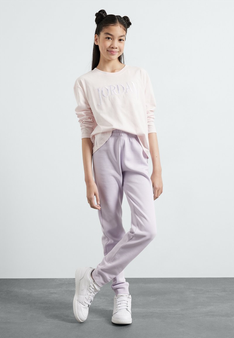 Camicia a maniche lunghe rosa chiaro con "JORDAN" ricamato in bianco, abbinata a pantaloni tuta lavanda e scarpe da ginnastica bianche. Design semplice, vestibilità casual.