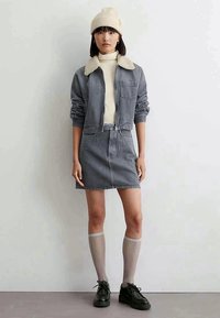 Denim jacket with a shearling collar, striped pattern, paired with a matching denim skirt. Model wears knee-high socks and black shoes.