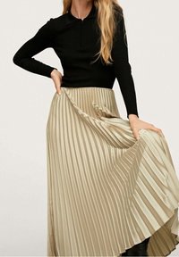 Un haut noir à manches longues côtelé associé à une jupe maxi plissée beige, mettant en valeur des plis verticaux et une texture fluide.