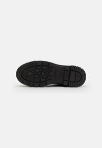 Semelle de chaussure en caoutchouc noir avec un motif de grip texturé, présentant une section centrale surélevée et des bords arrondis pour la durabilité et l'adhérence.