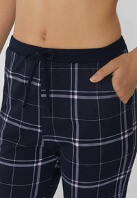 Marineblauwe geruite joggers met lichtroze lijnen, voorzien van een drawstring taille en zijzakken. Zachte stof met een gladde textuur.