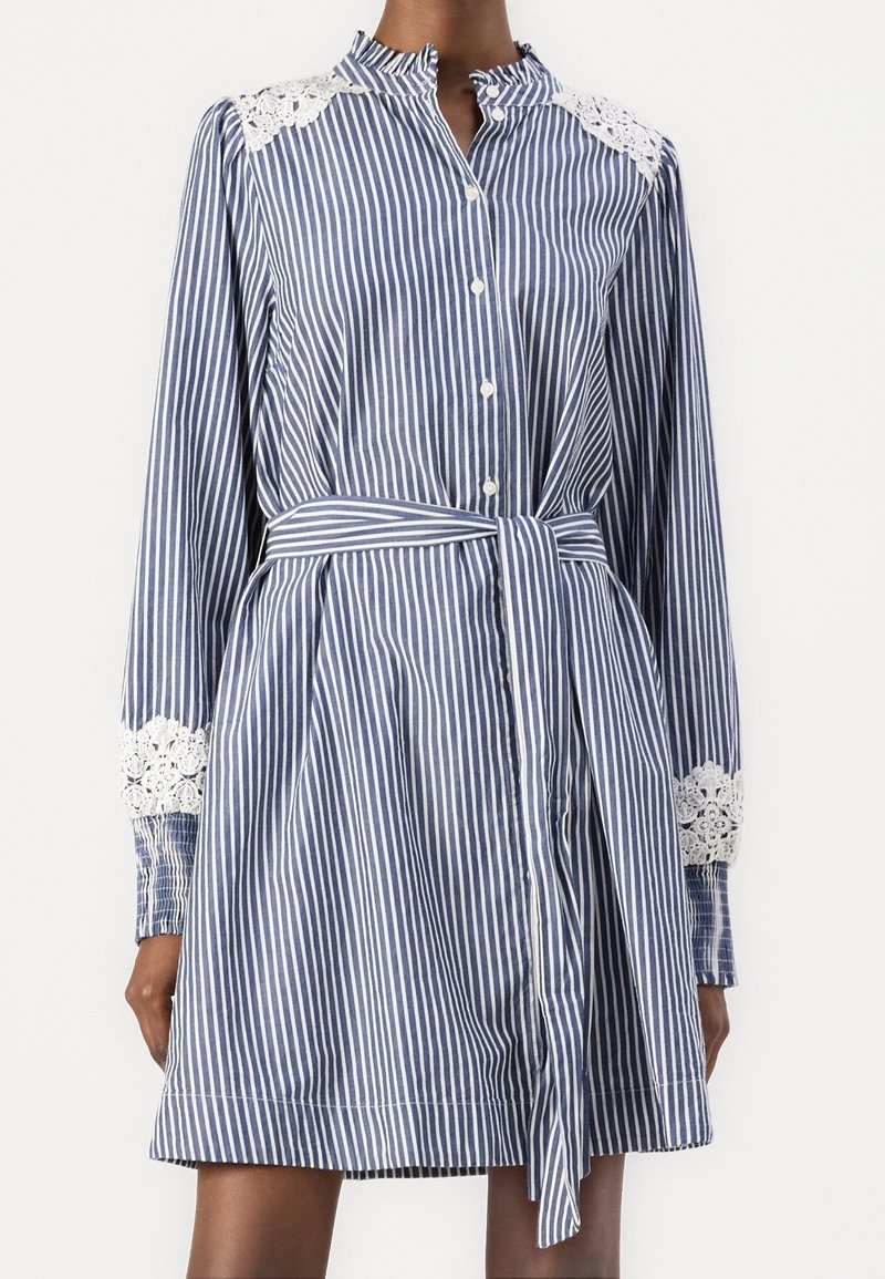 Randig blå och vit skjortklänning med långa ärmar, spetsdetaljer på axlarna, knäppning fram och knytbar midjebälte.
