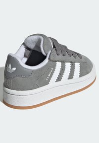 Zapatilla de ante gris con diseño de tres franjas blancas, acentos texturizados y suela de goma. Presenta un cuello acolchado y cierre con cordones.