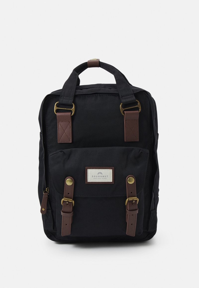 Sac à dos rectangulaire noir avec des bretelles en cuir marron, des boucles en laiton et une poche avant étiquetée "Doughnut."