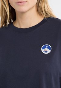 T-shirt en coton bleu marine avec encolure ronde et manches courtes. Comprend un logo circulaire brodé avec des montagnes et une étoile en bleu et blanc.