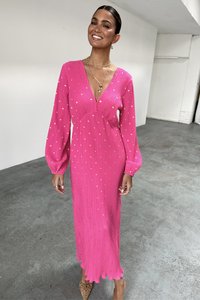 Pink, long-sleeve dress featuring a deep V-neck, textured fabric with gold dots, and a scalloped hem, worn with layered necklaces.