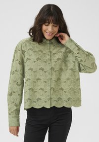 Blouse en coton vert avec un motif de broderie florale, fermeture à boutons sur le devant, ourlet festonné, manches longues et coupe décontractée.