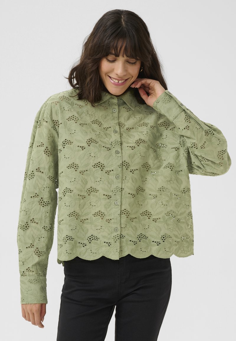Blouse en coton vert avec un motif de broderie florale, fermeture à boutons sur le devant, ourlet festonné, manches longues et coupe décontractée.