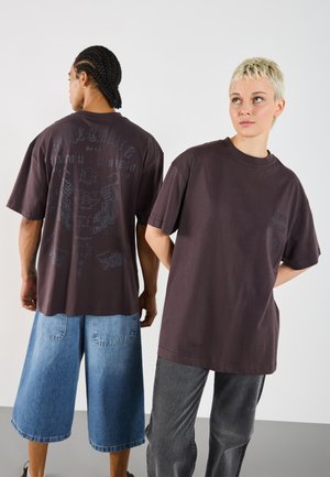Oversized dark brown graphic T-shirt featuring a design on the back, paired with light blue denim shorts and dark gray jeans.