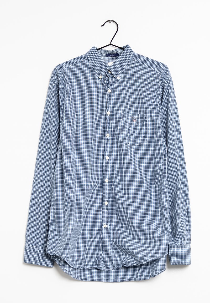 Chemise à manches longues boutonnée à petits carreaux bleus et blancs, avec poche avant, suspendue à un cintre noir sur fond blanc.