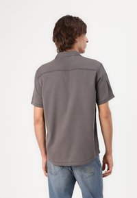 Chemise à manches courtes, grise, en tissu texturé, avec un col pointu et des coutures renforcées dans le dos.