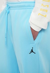 Gaiši zili sporta bikses ar aukliņu jostasvietā, sānu kabatām un melnu Jordan logo uz kreisā augšstilba. Gluda auduma apdare ar brīvu piegriezumu.