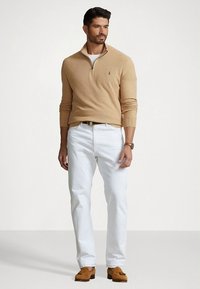 Tan pulover z zadrgo na vratu čez belo majico, kombiniran z belimi hlačami in rjavimi loaferji. Iz volnenega materiala, oprijet kroj, rebrasti robovi.