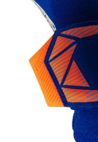 Close-up van blauwe stof met oranje en blauwe geometrische rubberen patronen, met een zeshoekige oranje label met gestructureerde lijnen en merknaam.