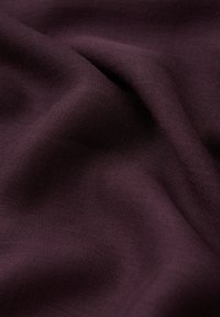 Tissu de couleur prune profonde avec un tissage doux et texturé, présentant de légers plis et ondulations, mettant en valeur son drapé naturel et sa qualité.