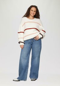Weißer, flauschiger Pullover mit pinken und roten Streifenmustern, kombiniert mit weit geschnittenen blauen Jeans und silbernen Schuhen.