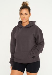 Dunkelgrauer Hoodie aus weichem Stoff, mit einer Fronttasche, gerippten Bündchen und einer Kordelzugkapuze. Es wird mit schwarzen Shorts kombiniert.