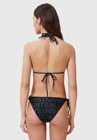 Czarny bikini z dekoltem halter, z zapięciami na wiązania. Dół zdobi duży napis "SAINTS" w powtarzającym się wzorze. Gładka tekstura.
