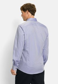 Light purple button-up shirt with a small geometric pattern, long sleeves, and a classic collar; fitted design with rounded hem.