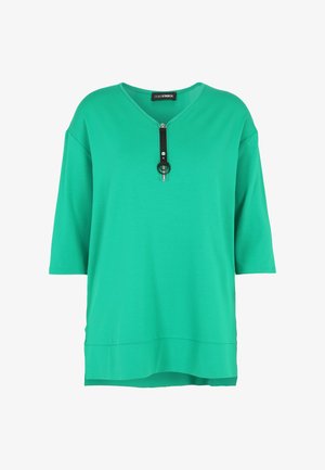 Green, short-sleeve top featuring a V-neck and a decorative zipper with a black strap and circular accent. Made from a soft, smooth material.