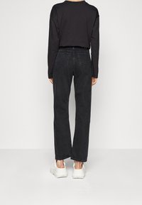 Jeans de denim negro con un corte relajado y pierna recta, combinados con una camiseta de manga larga negra y zapatillas gruesas blancas.