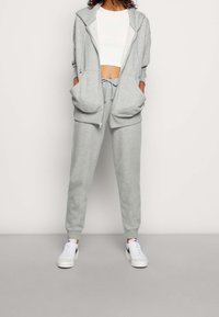 Ljusgrå bomullshuvtröja med stora framfickor, kombinerad med matchande sweatpants och vita sneakers, med en avslappnad passform.