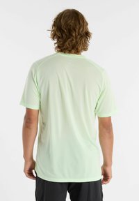 Vihreä urheilupaita, jossa on verkkomainen rakenne, lyhyet hihat ja kontrastiväriset saumat. Sisältää pyöreän kaula-aukon ja lievät sivureiät.