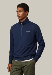 Maglione blu navy con mezza cerniera, interno del colletto bianco e sottile logo "HACKETT". Tessuto morbido in misto cotone e vestibilità comoda.