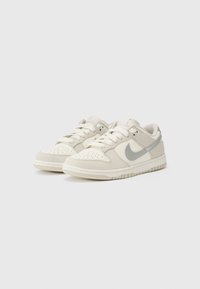 Lysegrå og cremefarvede lavtop sneakers, lavet af læder og ruskind, med perforeret tå, snørebånd fortil og et sølvfarvet Nike swoosh logo.