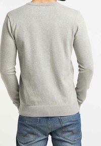 Grauer Strickpullover mit langen Ärmeln, rundem Halsausschnitt, Nahtdetails und Rippbündchen, getragen über blauen Jeans mit Rückentaschenstich.