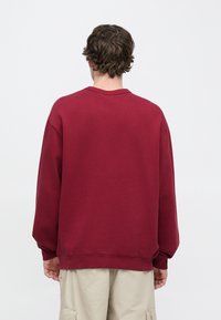 Μπορντό φούτερ με χαλαρή εφαρμογή, κατεβασμένους ώμους, ριμπ μανσέτες και τελείωμα. Λείος υφασμάτινος χαρακτήρας, απλό σχέδιο και λαιμόκοψη τύπου μπλούζας.