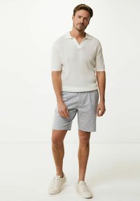Weißes, strukturiertes Poloshirt mit kurzem Ärmel und V-Ausschnitt; hellgraue, gemusterte Shorts; weiße Sneakers. Minimalistische und neutrale Farbpalette.