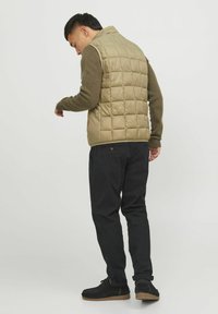 Beige, quiltēta, bez piedurknēm pūkainā veste ar ribotu brūnu piedurkni, apvienota ar melnām sašaurinātām biksēm un melnām zamšādām potīšu zābakiem.