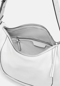 Sac à main en cuir blanc à la texture douce, avec des accents noirs, un compartiment principal zippé et une poche intérieure avec une languette.