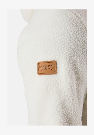 Kurtka polarowa w odcieniu kremowym z teksturowaną, pluszową powierzchnią. Posiada brązową skórzaną naszywkę z logo SWEDEMOUNT na rękawie.