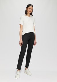 Camiseta blanca de manga corta con logo azul, combinada con jeans negros ajustados y zapatillas blancas con suelas texturizadas. Diseño simple y moderno.