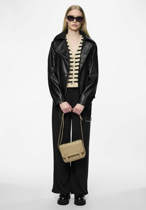 Giacca di pelle nera sopra un cardigan beige a righe, pantaloni larghi neri, scarpe con piattaforma nere e una piccola borsa a tracolla beige.