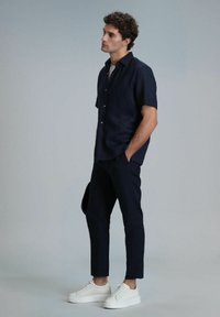Marineblauwe korte mouw shirt van een lichtgewicht stof, gecombineerd met smal gesneden donkere broeken en witte sneakers. Opvallende details zijn een subtiele textuur.