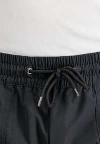 Nära bild av svart elastisk midjeband med knytdragband på byxor mot en vit tygbakgrund.