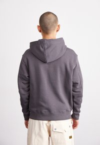 Hanorac gri dintr-un amestec moale de bumbac, având o glugă mare, manșete ribbate și un croi lejer. Purtați-l cu pantaloni de culoare deschisă.