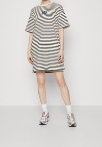Gestreiftes T-Shirt-Kleid in Creme und Marineblau, mit kurzen Ärmeln und rundem Ausschnitt. Dazu kommen sportliche Sneakers und weiße Socken.