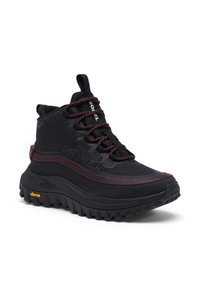 Botte noire montante imperméable avec tissu texturé, accents rouges contrastants, semelle épaisse en caoutchouc noir et semelle à motif antidérapant.