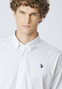 Camicia bianca con bottoni e colletto classico, realizzata in tessuto di cotone, con logo ricamato in blu navy sul petto sinistro.