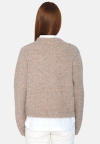 Beige strikket genser med kort lengde, ribbestrikket kant og myk tekstur, brukt over en hvit skjorte med krage. Bakfra vises.