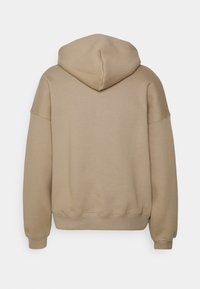 Mikina s kapucí světle hnědé barvy, s volným střihem, žebrovanými manžetami a lemem a hladkou, měkkou texturou. Vidět zezadu.