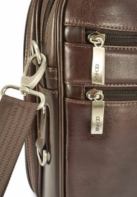 Brązowa skórzana torba z dwiema komorami na zamek błyskawiczny, metalowymi ozdobami oraz odpinanym materiałowym paskiem na ramię. Widoczna faktura powierzchni.