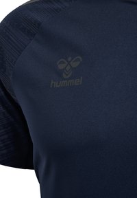 Camisa deportiva azul marino con tejido texturizado en los hombros y un sutil logo de Hummel en un tono contrastante en el pecho.